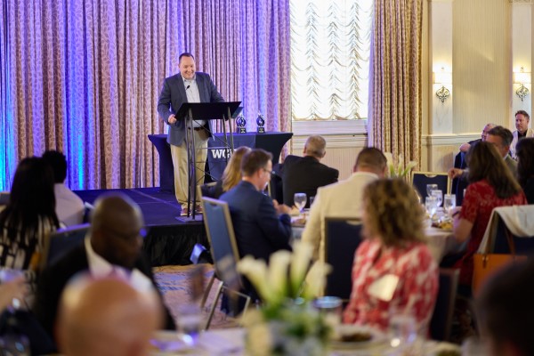 An event setting with a speaker at a podium and attendees at dinner tables.