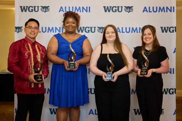 Four alumni pose proudly with their awards in front of a WGU banner.