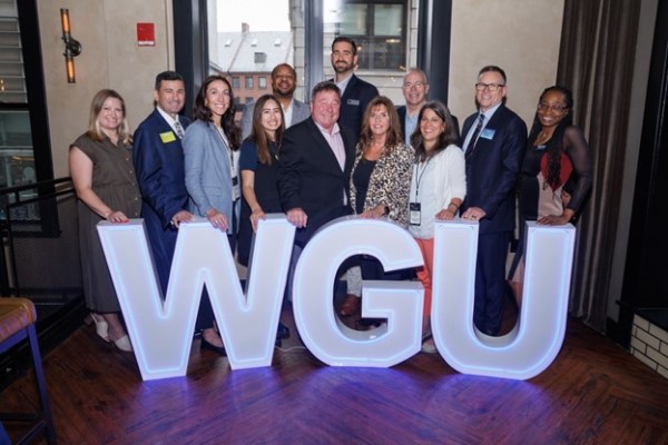 A group of diverse professionals smiling behind large illuminated letters spelling "WGU".