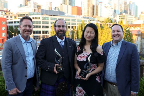 Four people, including two award recipients, stand smiling against a city skyline backdrop.