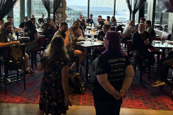 A group of people gathered in a restaurant or bar setting, with some seated at tables and others standing.