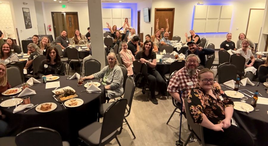 A large group of people smiling and interacting at an evening dinner.