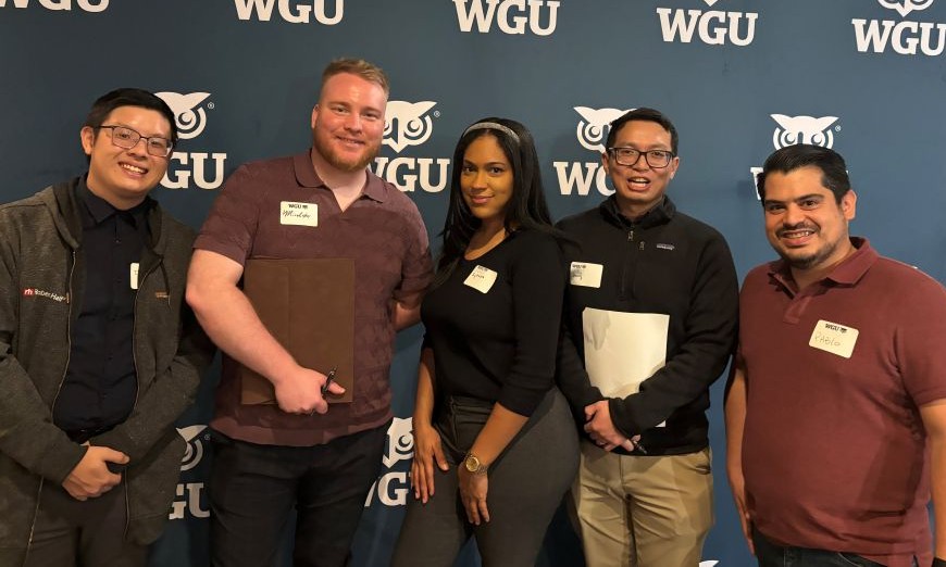 Five smiling individuals, including three men and two women, pose in front of a blue WGU-branded backdrop with owl logos.