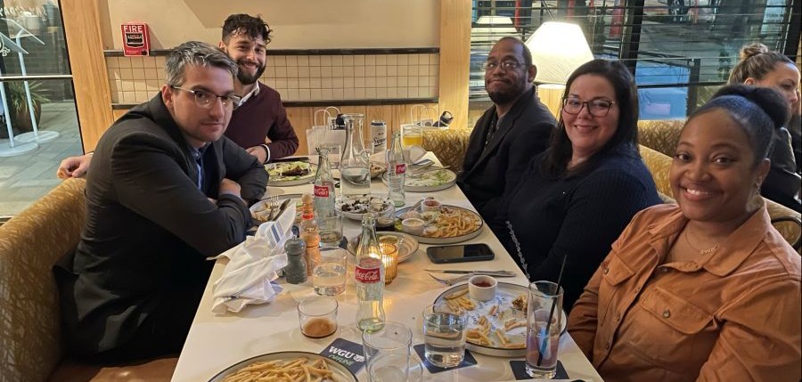 A group of six diverse individuals, three men and three women, happily dining together at a restaurant table filled with plates of food and drinks.