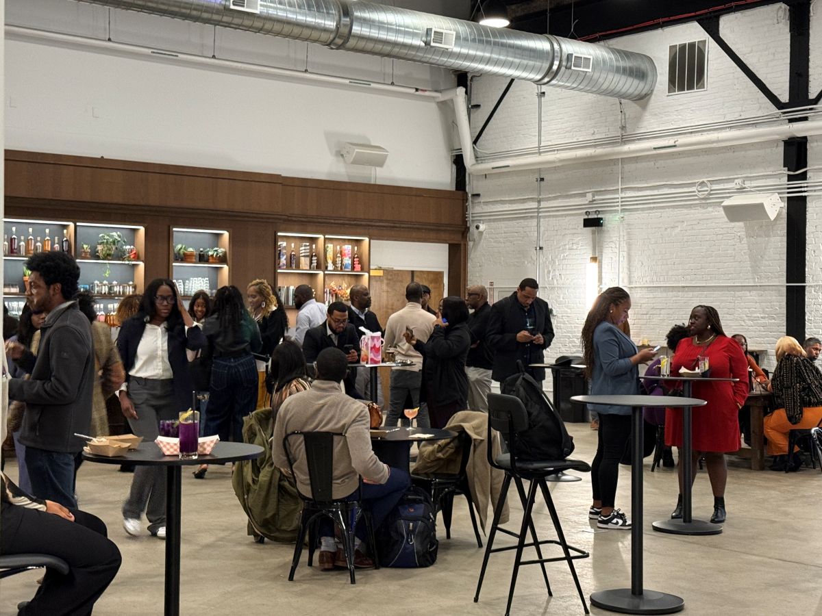 A large group of people socializing and networking at an indoor event with high-top tables and drinks.
