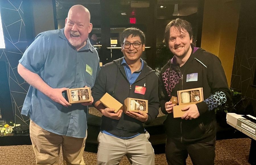 Three smiling men holding gift boxes, looking happy to receive their presents at an event.