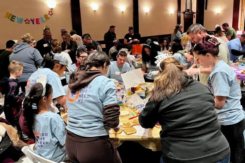 An indoor scene showing numerous individuals engaged in a collaborative activity, with several wearing light blue t-shirts and some sporting festive New Year's accessories.