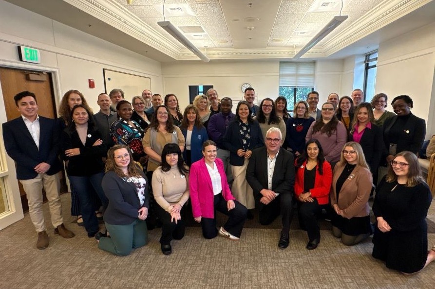 A large, diverse group of smiling people, some standing and some kneeling, posing for a photo in an indoor setting.
