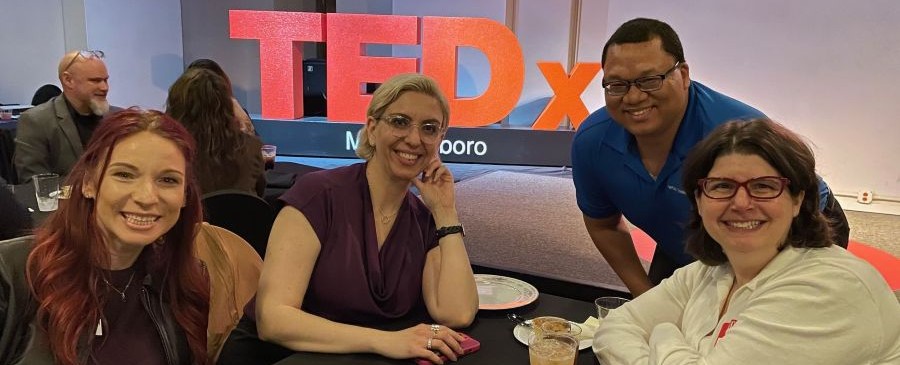 Four smiling attendees at a TEDx event, with the large red 'TEDxMurfreesboro' sign visible in the background.