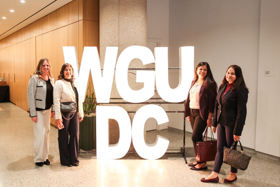 Four women posing in front of large, illuminated letters spelling out 'WGU DC' at an indoor event.