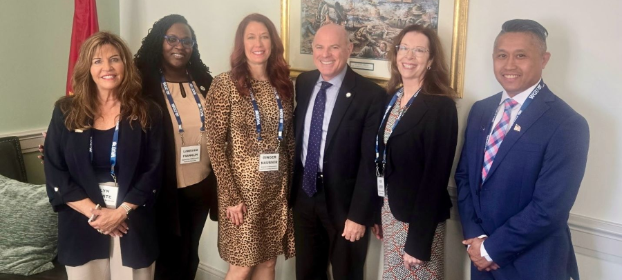 A group of six people, dressed in business casual attire and lanyards, posing for a photo in a professional setting.