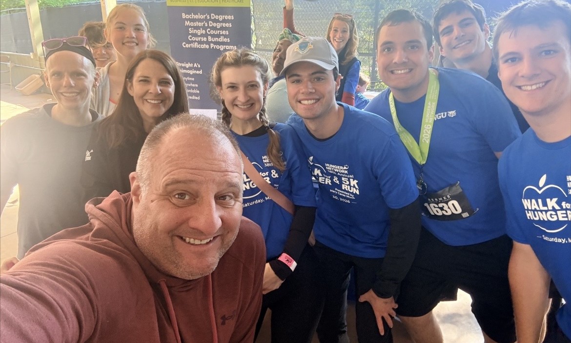 A large group of smiling people, many wearing blue t-shirts from a 'Walk for Hunger,' posing for a selfie.