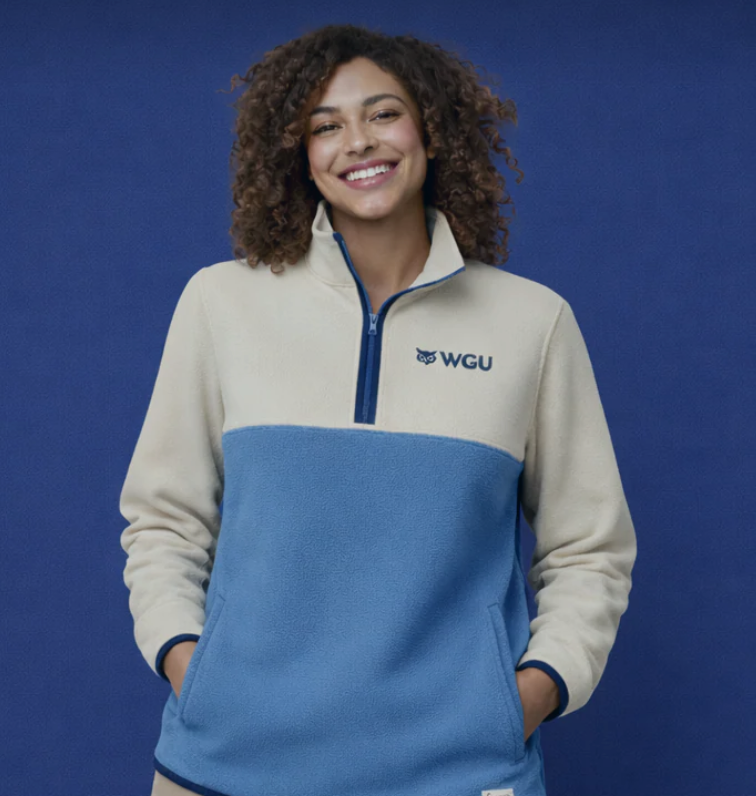 A smiling woman with curly hair wears a two-tone cream and blue fleece pullover with a 'WGU' owl logo.