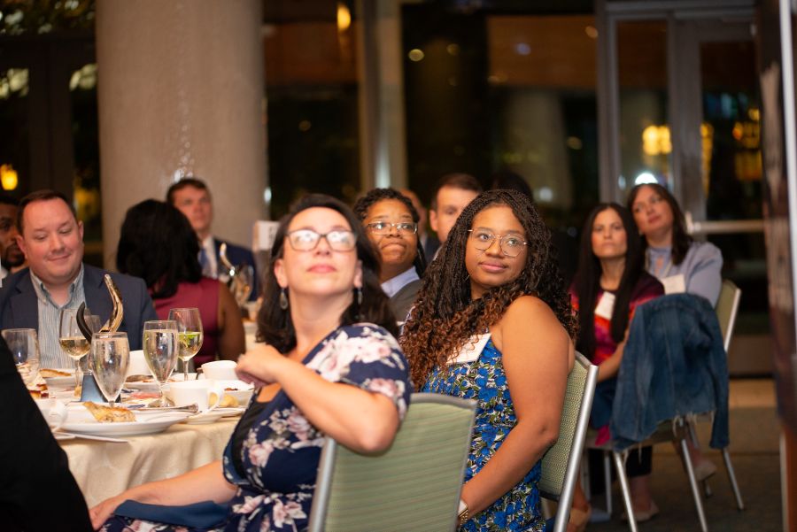 A diverse group of attendees seated at tables, attentively watching an event.