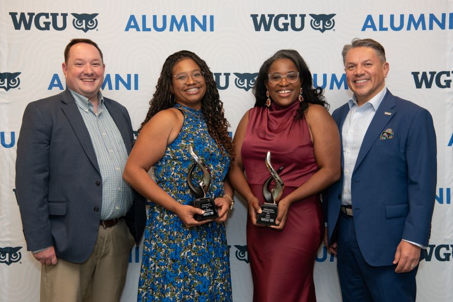 Four individuals, two men and two women, smiling and posing with awards in front of a "WGU Alumni" backdrop.