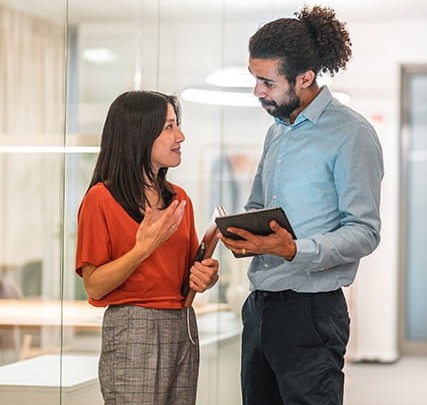 Two professionals, a woman and a man, discussing work in a modern office environment.