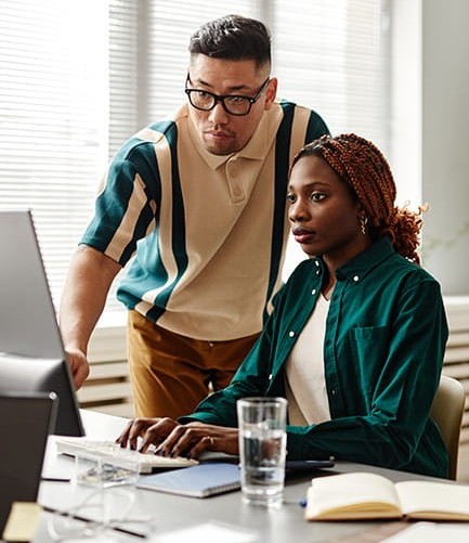 Two colleagues, a man and a woman, collaborating and looking intently at a computer screen.