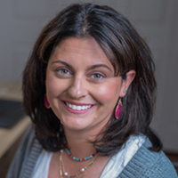 Portrait of a friendly woman wearing a gray sweater and colorful jewelry.