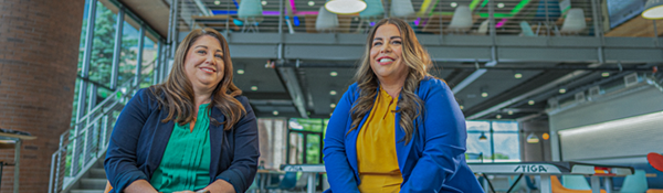 Two women are seated and smiling in a bright, open office space.