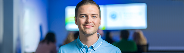 A man in a blue shirt smiles at the camera in front of a business presentation