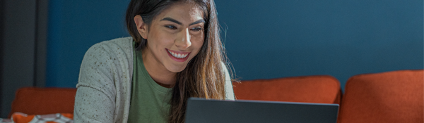 A woman smiles while looking at her laptop.