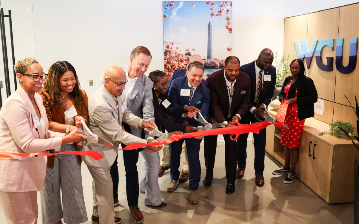 Community leaders use oversized scissors to cut a red ribbon during a WGU office opening celebration.